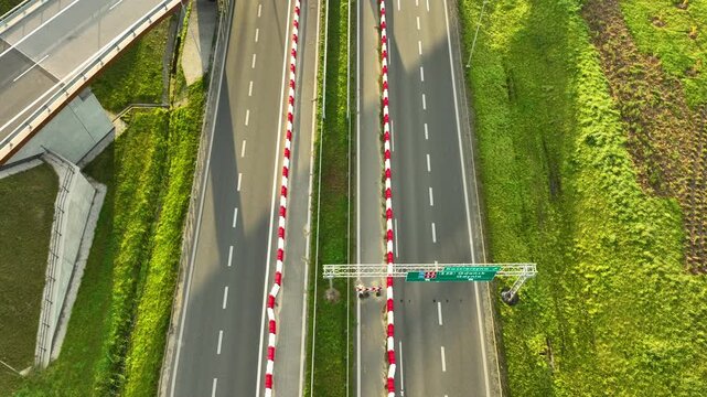 Close top-down drone view of the S6 expressway lanes, showing a white car passing beneath an overhead road sign gantry, framed by red and white barriers