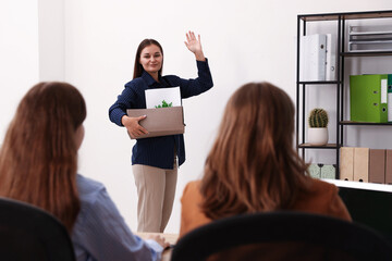 Woman with stuff waving goodbye to her colleagues in office