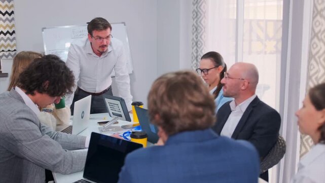 Determined business analyst conducts a high-priority meeting on a sudden market spike, guiding the team toward fast and effective decisions. Colleagues with laptops collaborate in a modern office.