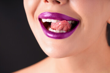 Woman with beautiful purple lipstick on her lips against black background, macro view