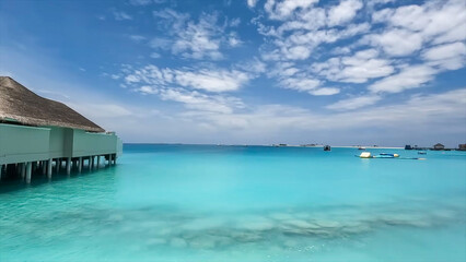 Open view of bright turquoise ocean with white foam and water toys, next to overwater bungalows under cloudy blue sky