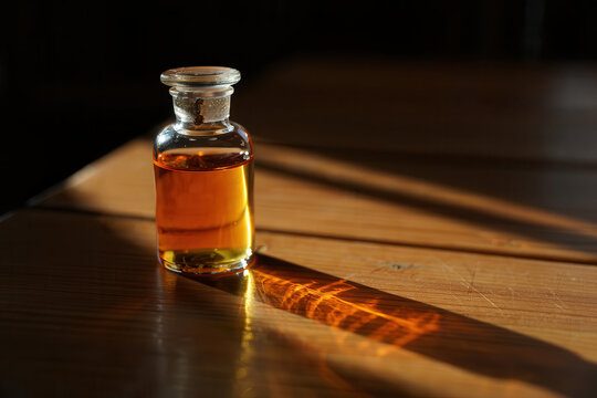 A small glass bottle filled with amber liquid casts a long shadow across a textured surface in dramatic lighting