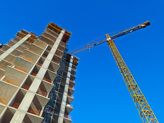 wide shot of a yellow tower crane next to a concrete high-rise building under construction against...