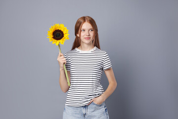 Teenage girl with beautiful sunflower on grey background