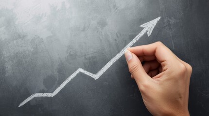 A high-angle, close-up shot of a person's hand completing the drawing of a jagged, upward-sloping graph line, culminating in a large arrow head, on a textured, dark gray or black chalkboard.