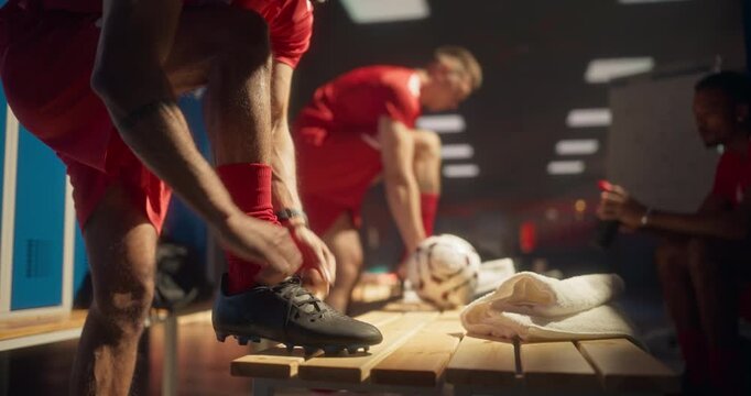 Soccer Athlete in Sports Red Outfit Bending Down to Tighten Laces on His Shoes in a Close Up View. Teammates Around Continue Their Pre-Match Preparation, Getting Ready for a Championship Game