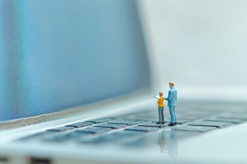 Miniature figures explore a vast laptop keyboard and screen, symbolizing digital learning, online education, and technological guidance in a connected world.