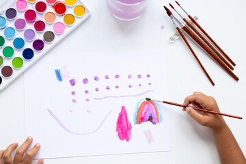 Creative child painting with watercolors and brushes on white paper