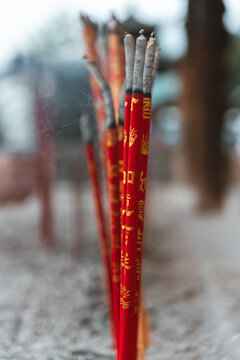 View of vibrant red incense sticks adorned with golden Chinese characters rise from a bed of ash in a temple, a wisp of smoke dancing, Dali, Yunnan, China.