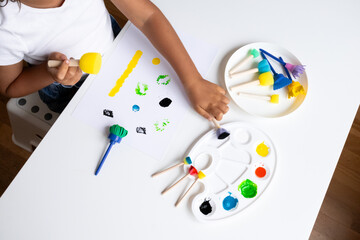 Child engaging in creative painting with colorful art supplies on white table