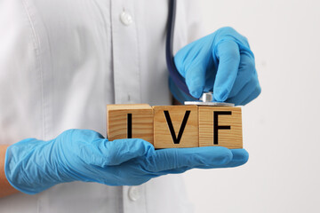 In vitro fertilization. Doctor holding wooden cubes with abbreviation IVF against white background,...