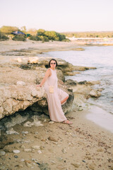 A woman in a long dress stands near the rocks on the seashore, boho style