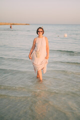 A woman in a long dress stands in the sea, summer seaside vacation