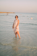 A woman in a long dress stands in the sea, summer seaside vacation