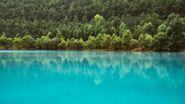 Fototapeta View of a tranquil turquoise lake mirroring the lush, green forest canopy above, creating a serene and vibrant natural scene, Lijiang, Yunnan, China.