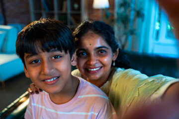 Indian Child and mother capture fun selfie on sofa, showing love and family bonding indoors