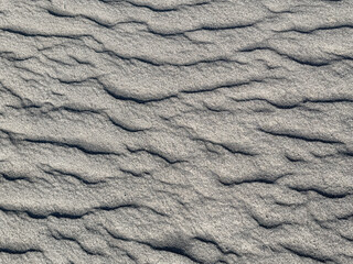 Close up of grey sand texture with random rippled steam and wavy pattern. As a result of wind abrasion and sand storm forming this 3d contour and pattern. Seamless background texture.