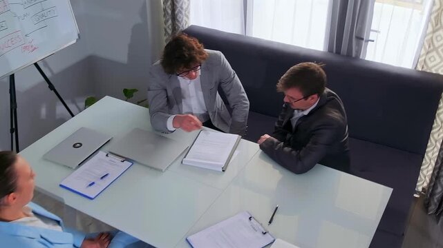 Corporate director and legal advisor discuss contract details across from an assistant in a bright modern office. Professional teamwork, corporate strategy, and legal consultation with documents.