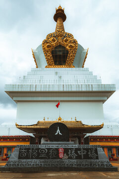 View of a white stupa adorned with intricate golden details stands majestically against a cloudy sky, a serene monument of faith, Di Qing Zang Zu Zi Zhi Zhou, Yun Nan Sheng, China.
