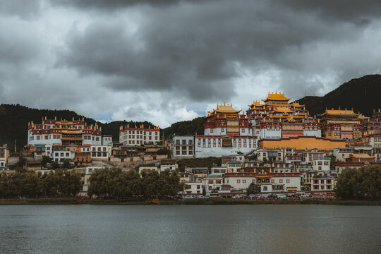 View of Tibetan-style architecture cascading down the hillside, a symphony of white walls and golden roofs against a backdrop of moody skies, Di Qing Zang Zu Zi Zhi Zhou, Yun Nan Sheng, China.