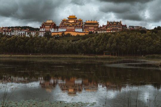 View of the golden-roofed monastery stands proudly against a stormy sky, mirrored in the tranquil waters of a lake, Di Qing Zang Zu Zi Zhi Zhou, Yun Nan Sheng, China.