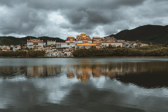 View of golden roofs glinting atop the monastery complex reflected on the still lake under a brooding sky, Di Qing Zang Zu Zi Zhi Zhou, Yun Nan Sheng, China.
