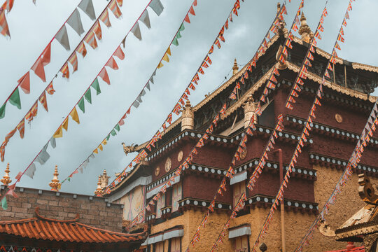 View of vibrant prayer flags strung across the sky, framing a traditional Tibetan building with intricate gold details and red accents, Di Qing Zang Zu Zi Zhi Zhou, Yun Nan Sheng, China.