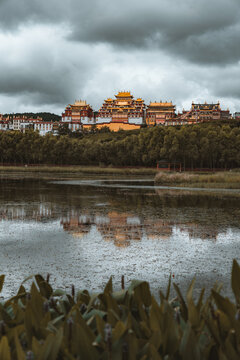 View of golden roofs gleam under a stormy sky, reflected in the tranquil waters, a serene contrast of nature and architecture, Di Qing Zang Zu Zi Zhi Zhou, Yun Nan Sheng, China.
