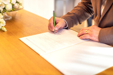 A man signs a marriage contract with a pen at an office or church. Confirmation of a surname change by signature at a wedding day