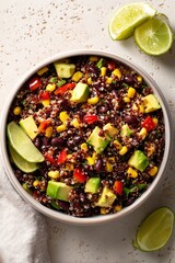 Mexican quinoa black bean salad with corn, avocado, and bell peppers in white bowl with lime