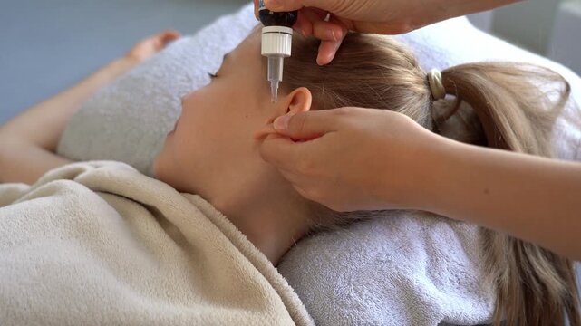 Mothers hands drips into ear ear drops of little girl from otitis. Ear pain medication. Childhood diseases. Virus infection cold flu illness