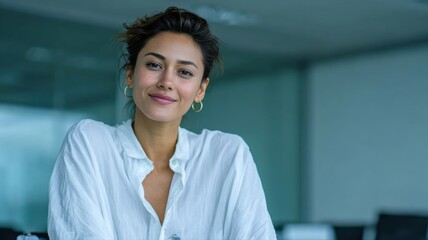 young Indian female executive sitting in a modern office wearing a white formal shirt and gold earrings