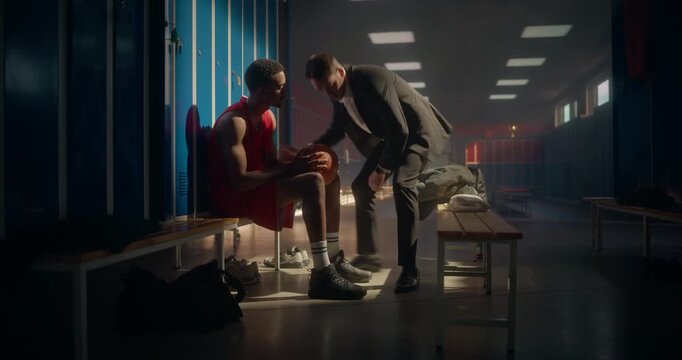 Young African American Basketball Athlete Sitting with Head Down, Feeling Frustrated in the Locker Room. Coach Joins Him, Placing a Hand on His Shoulder and Sharing a Reassuring Gesture