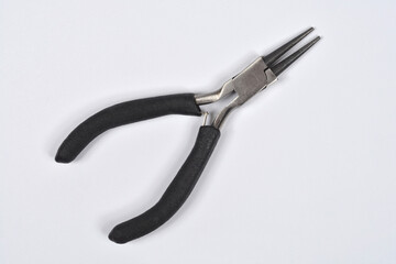 A close-up studio shot shows a pair of round-nose pliers with black rubber handles on a neutral...