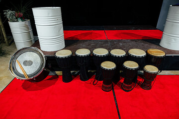 A line of traditional African djembes and a bass drum arranged on a red carpet stage, showcasing handcrafted design and cultural percussion instruments