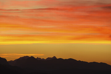 View of dark, brooding mountains etched against a fiery canvas of orange and yellow sky as the sun dips below the horizon, Aflenz, Steiermark, Austria.