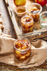 Homemade apple chutney in glass jars with visible chunks of apple, pear, dried fruit, ginger, and spices. Preserved autumn condiment on a rustic wooden background, perfect for seasonal cooking