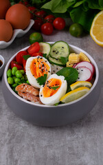 Poke bowl with smoked redfish, eggs, vegetables, edamame beans and rice served on gray table. Healthy balanced meal with white fish