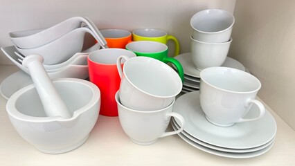 Tableware empty white porcelain cups and saucers with colorful designs for coffee or tea on a kitchen shelf. 