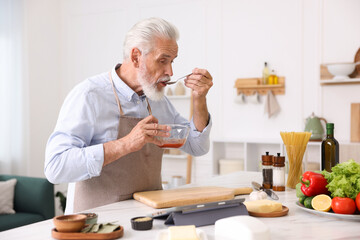 Elderly man cooking at white marble table in kitchen