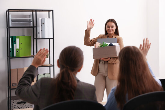 Woman with stuff waving goodbye to her colleagues in office