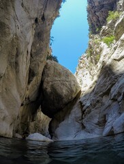 Majestic canyon walls with a giant rock suspended above the narrow river passage. Dramatic natural landscape showcasing rugged stone cliffs and clear blue sky.