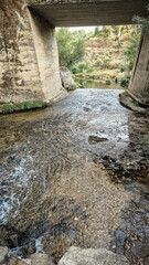 Clear Tinhela River flows beneath a concrete bridge at Praia Fluvial Rebelos near Murca, Tras-os-Montes, Portugal. Natural banks, tranquil water, and wild landscape invite peaceful leisure.