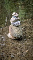 Stacks of balanced river pebbles on the water’s edge symbolize harmony, peace, and focus. Reflective surface and smooth stones evoke zen, mindfulness, and natural art.