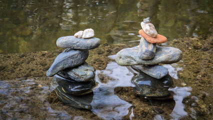 Stacks of balanced river pebbles on the water’s edge symbolize harmony, peace, and focus. Reflective surface and smooth stones evoke zen, mindfulness, and natural art.