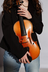 Female musician holds a violin while wearing a black blazer and light blue jeans in a studio setting