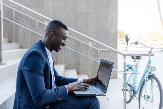 Young Businessman or student sitting on staircase working on laptop with bicycle nearby