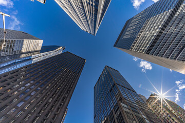 Street level view of highrise buildings with sunburst at 6th Ave & W 53rd St, Manhattan cityscape.