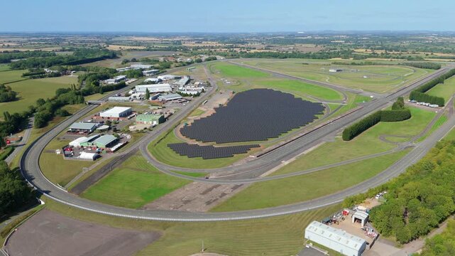Aerial view of a racetrack with a solar panel installation reflecting the sky, contrasting with the surrounding green landscape, Nuneaton, England, United Kingdom.