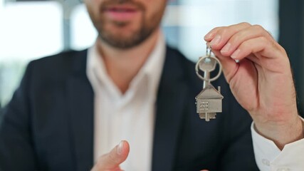 Smiling professional businessman in a black suit holds new house keys, symbolizing property ownership and successful real estate transaction at the office. - Powered by Adobe